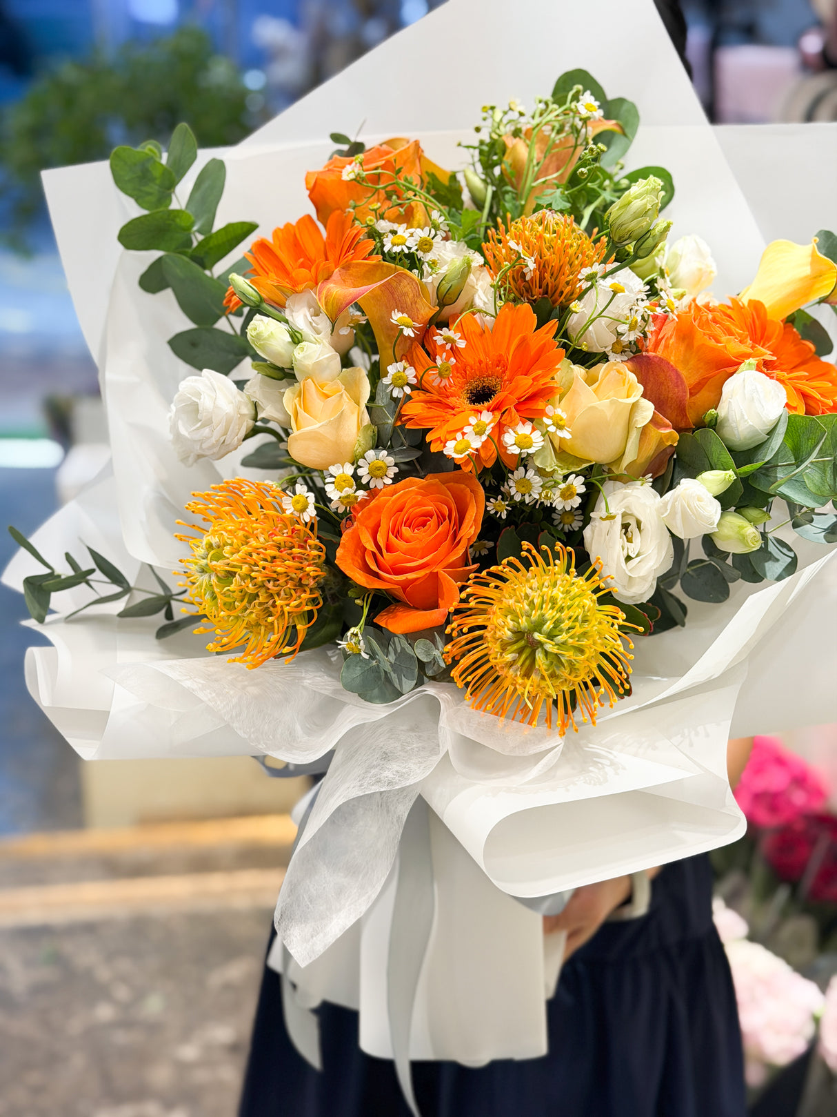 Reflower HK energetic bouquet featuring vibrant orange pincushion proteas, orange roses, gerberas, and chamomile, wrapped in crisp white paper, perfect for graduations and promotions.