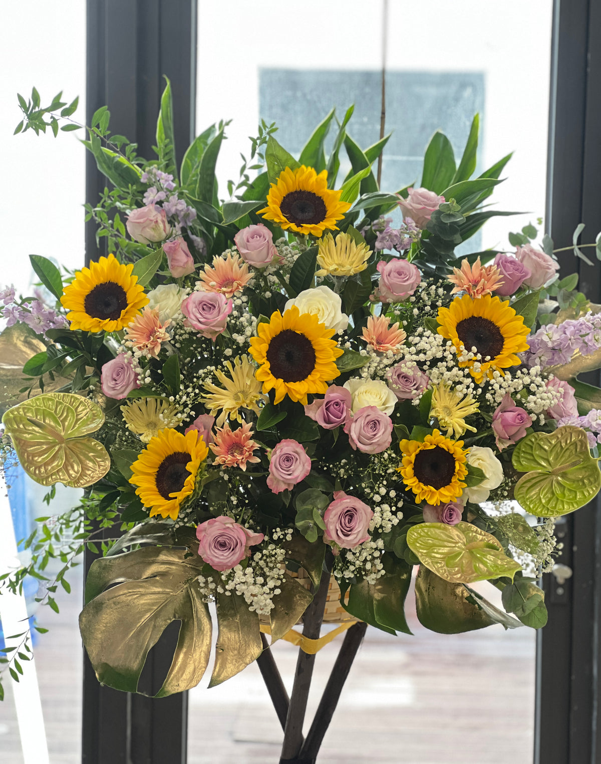 花點時間 Reflower 現代華麗開張花籃,以向日葵、紫玫瑰與太陽菊為主體,底部配搭金漆龜背葉與火鶴,祝賀新店開張大吉