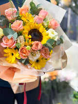 Reflower HK vibrant graduation bouquet featuring a bright sunflower, peach roses, and yellow gerberas, wrapped in warm peach paper, perfect for graduation photos and ceremonies.