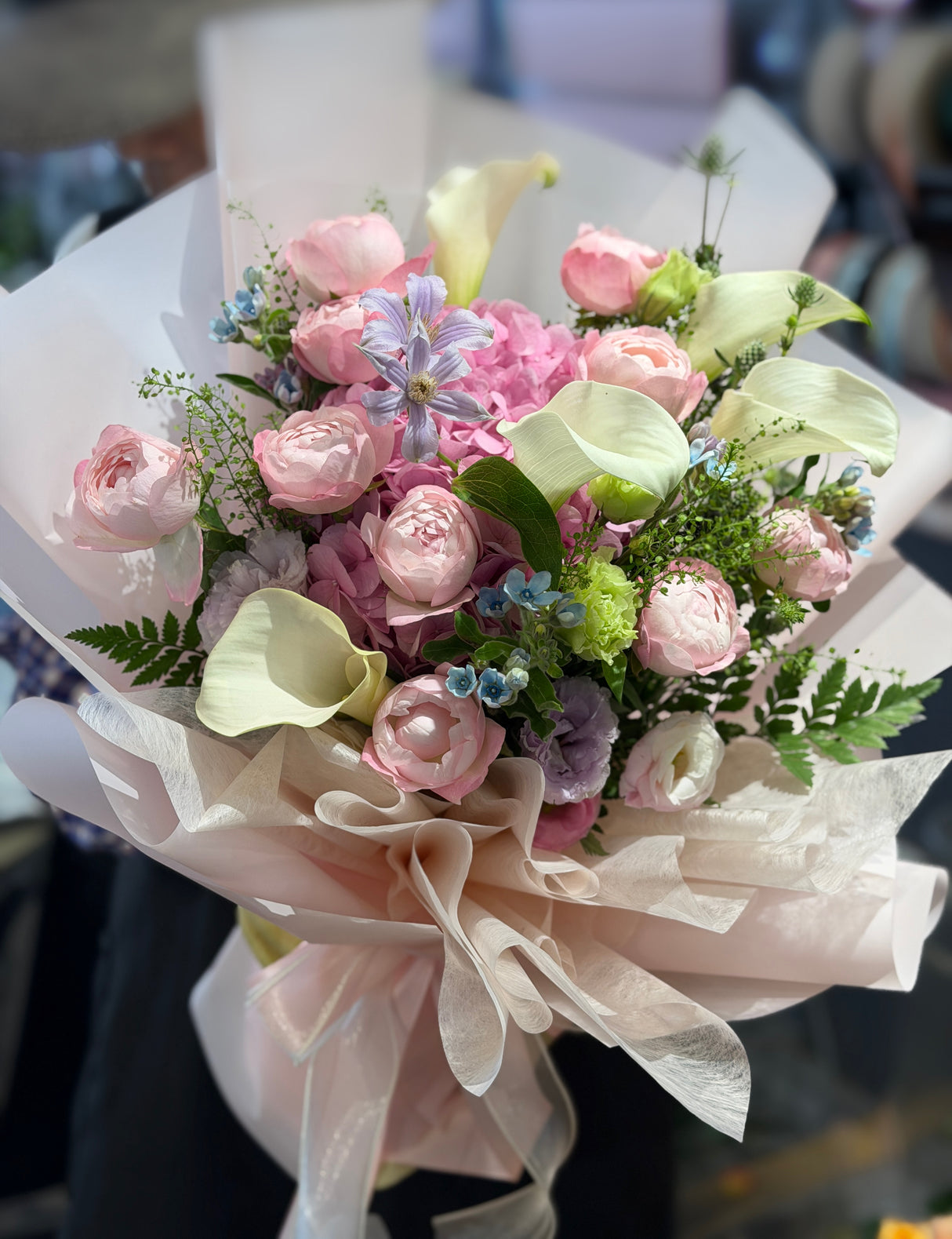 Reflower HK dreamy garden-style bouquet featuring a pink hydrangea, elegant white calla lilies, pink cup roses, and clematis, wrapped in nude-pink paper and wavy organza.