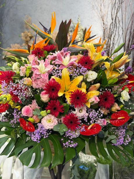 Reflower HK festive grand opening flower stand featuring Birds of Paradise, yellow and pink lilies, red gerberas, and anthuriums, accented with monstera leaves.