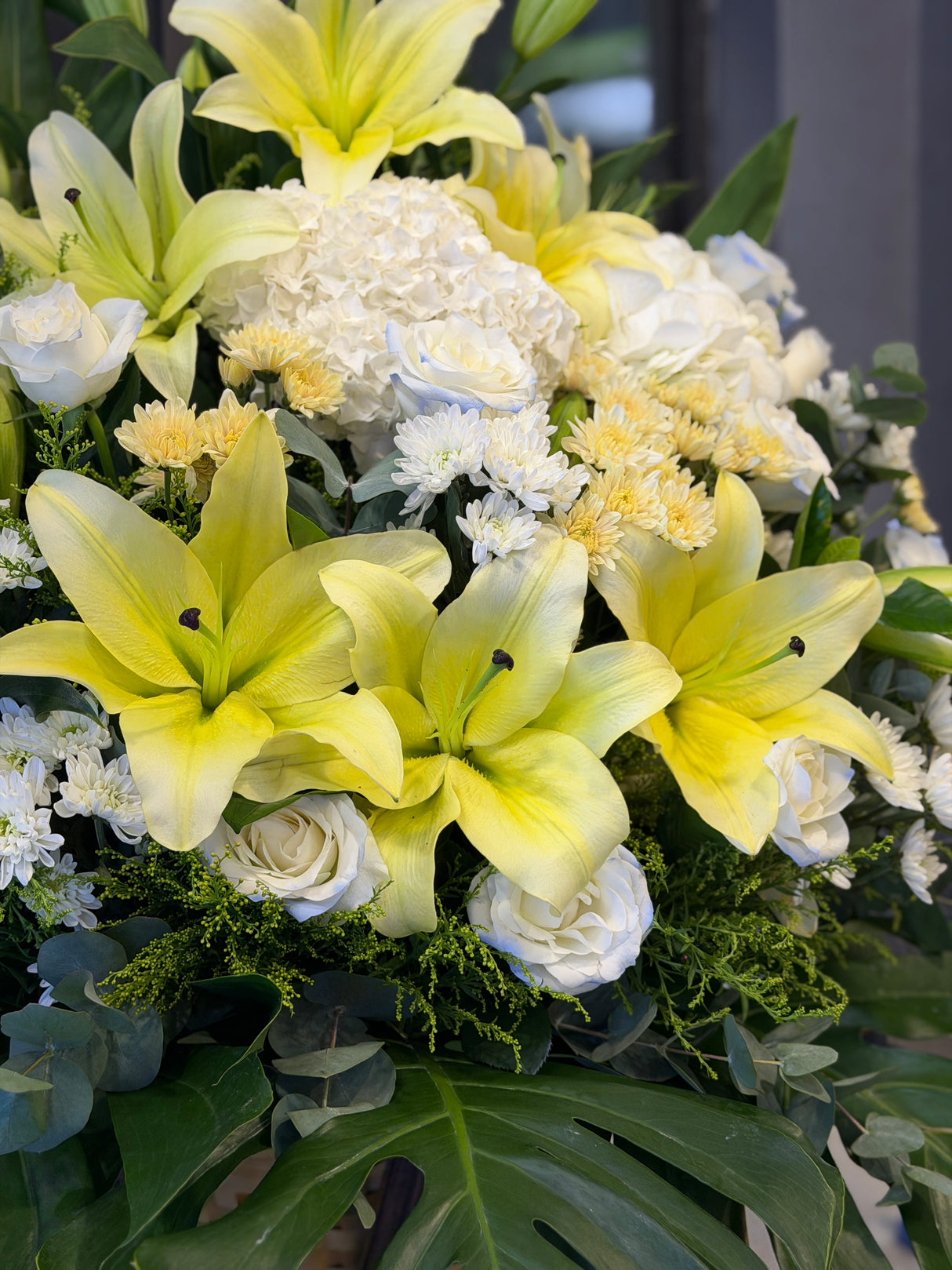 Reflower HK elegant sympathy flower stand featuring yellow lilies, a white hydrangea, ice blue roses, and chrysanthemums, designed for funeral homes and memorial services to express deepest condolences.