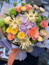 Reflower HK cheerful bouquet featuring a purple hydrangea, peach roses, and yellow spider gerberas, wrapped in elegant light purple paper with a peach ribbon.