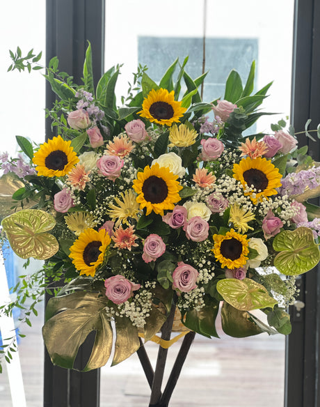 花點時間 Reflower 現代華麗開張花籃，以向日葵、紫玫瑰與太陽菊為主體，底部配搭金漆龜背葉與火鶴，祝賀新店開張大吉